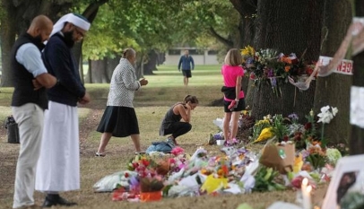People on Tuesday stand next to floral tributes placed across the road from the Al Noor Mosque in Christchurch, New Zealand, where dozens of worshippers were gunned down last week. Photo: MARTY MELVILLE / AFP/GETTY IMAGES