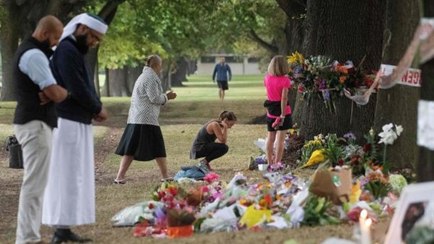 People on Tuesday stand next to floral tributes placed across the road from the Al Noor Mosque in Christchurch, New Zealand, where dozens of worshippers were gunned down last week. Photo: MARTY MELVILLE / AFP/GETTY IMAGES